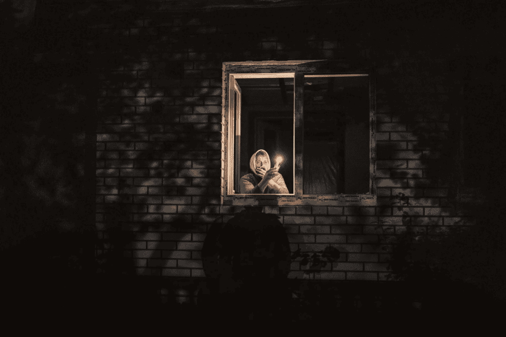 A person holding a small flame in a dark window of a brick building, reflecting the sombre reality of the Ukraine war.
