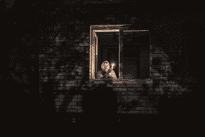 A person holding a small flame in a dark window of a brick building, reflecting the sombre reality of the Ukraine war.