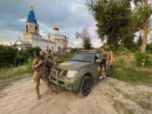 Ukrainian soldiers with a donated Protect Ukraine 4x4 vehicle in front of a church with a striking blue spire.