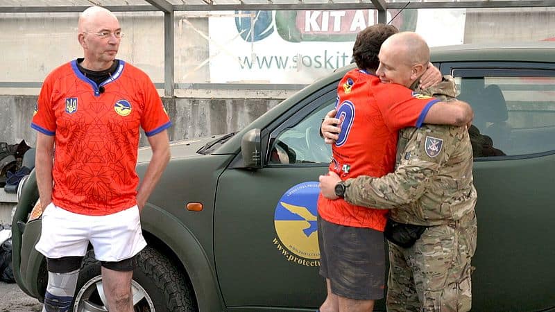 Author and Protect Ukraine ambassador Tommy Wieringa with a rugby player hugging a Ukrainian soldier, in front of a donated 4x4 vehicle with the Protect Ukraine logo.