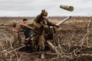 Soldiers operating an artillery gun during the war in Ukraine, with an empty shell casing flying mid-air.
