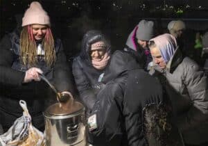 A volunteer distributing hot soup to elderly residents in freezing winter conditions.